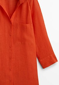 Långärmad orange linne skjorta med knappar fram, bröstficka till vänster och snibbkrage mot en vit bakgrund.