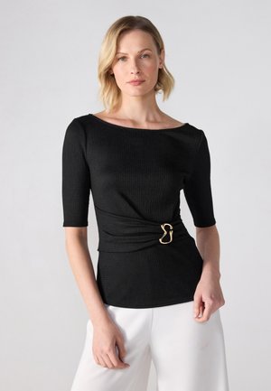 Musthave mustre tekstuuriga must pluus, millel on kolmveerandi varrukad, kullast detail vööl, sobitades valgete pükste juurde.
