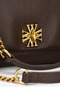 Hnědá kožená kabelka s výrazným zlatým emblémem a kováním, texturovaným povrchem a detailem řetízkového popruhu.
