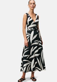 Schwarz-weißes Wickelkleid mit V-Ausschnitt, versehen mit einem Blattmuster, ärmellos und mit einem Gürtel in Taillenhöhe. Glatte Textur.