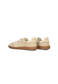 Tannfarbene Wildleder-Sneaker mit flauschigen cremefarbenen Textilakzenten, die drei weiße Streifen und eine strukturierte Gummisohle aufweisen, von der Seite und von hinten betrachtet.