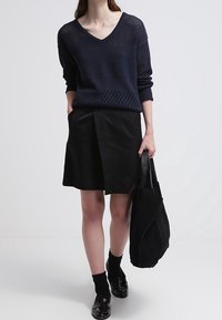 Tmavě modrý pletený svetr s výstřihem do V, kombinovaný s černou plisovanou sukní a černými ponožkami. Oblečení doplňuje černá semišová taška přes rameno.