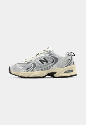 Grijze en witte sportschoenen gemaakt van mesh en synthetische materialen. Voorzien van een gevoerde zool, veters en een zichtbaar logo aan de zijkant.