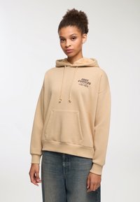 Beżowa bluza z kapturem z miękką, teksturowaną podszewką, przednia kieszeń typu kangur i czarny nadrukowany tekst "BEZPŁATNE PRZYTULANIE 1-264-9873." Długie rękawy.