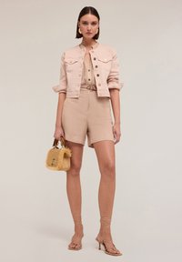 Giacca di jeans cropped rosa chiaro, pantaloni corti beige e tacchi a fascia color pelle. Borsa di paglia piccola con dettagli testurizzati. Tessuto liscio e design elegante.