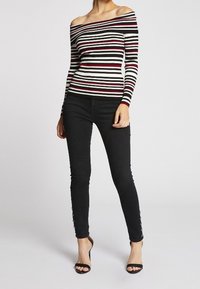 Sweter z odsłoniętymi ramionami w prążki w kolorach czarnym, białym i czerwonym, zestawiony z czarnymi obcisłymi spodniami ozdobionymi bocznymi guzikami oraz wysokimi obcasami.