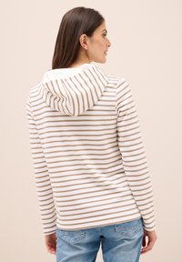 Sudadera a rayas en blanco y marrón claro, con capucha ajustable y mangas largas, combinada con jeans de denim azul.