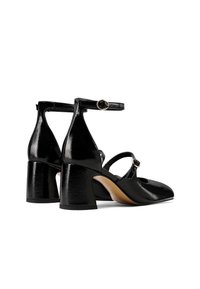 Scarpe con tacco in pelle verniciata nera, con cinturini alla caviglia e punta arrotondata. Tacco a blocco spesso e una lieve lucentezza sulla superficie.