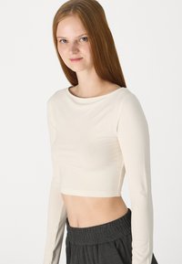 Un haut crop en crème à manches longues avec un col rond et une texture lisse, associé à un pantalon de jogging à taille élastique gris foncé.