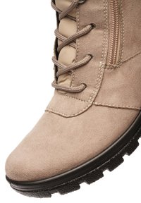 Beige suède wandelschoen met ronde neus, bruine veters, zijrits, gevoerde tong en zwarte textuurlzool.