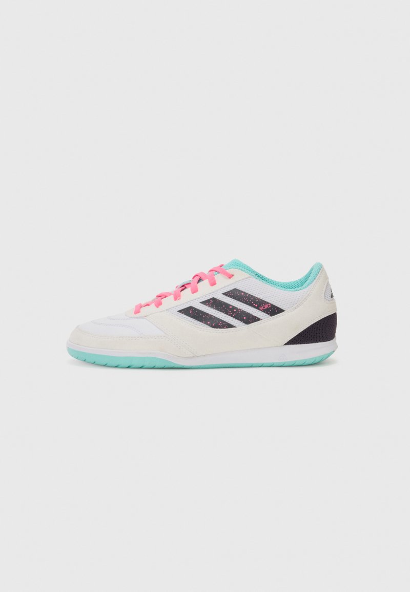 Vit träningsskor med rosa snören, tealaccent och svarta logostripes. Har en texturerad ovandel och en ljus mintgrön gummisula.