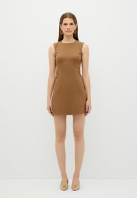 Brun ærmeløs kjole med en tætsiddende overdel og flicket nederdel, lavet af glat stof. Simpelt design, båret med beige slip-on sko.