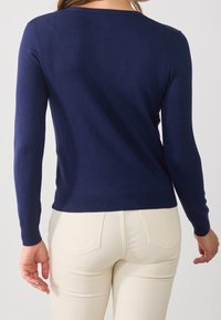 Mörkblå stickad tröja med långa ärmar, rund halsringning och ribbstickade fållar, kombinerad med ljusfärgade figurnära byxor.