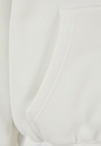 Tissu de sweat-shirt blanc avec une texture douce, avec une poche kangourou et des coutures renforcées le long des bords.