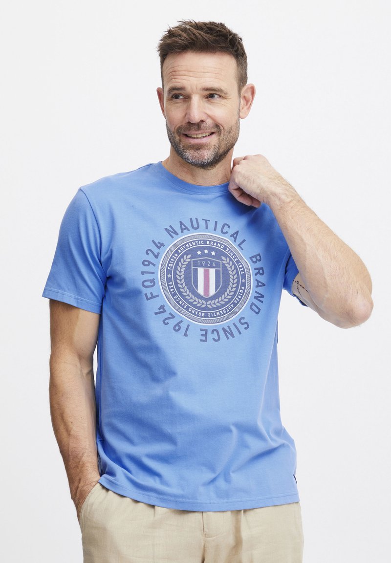 Lyseblå bomull T-skjorte med rund grafisk trykk som har teksten "Nautical Brand Since 1924" og dekorative detaljer. Korte ermer, rund hals.