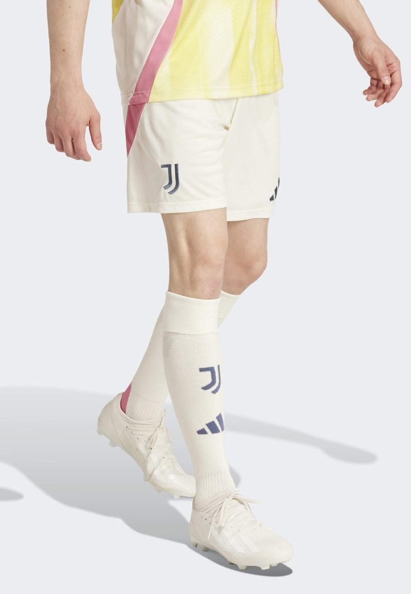 Valkoiset jalkapallosortsit, joissa on tummansininen logo ja vaaleanpunaiset korostukset, yhdistettyinä valkoisiin sukkiin, joissa on logoja ja vaaleanpunainen raita, käytetään valkoisten nappulakenkien kanssa.