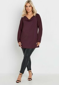 Burgundy topp med cowl-hals och långa ärmar, kombinerat med svarta läderleggings och svarta klacksandaler med remmar. Slät textur, avslappnad passform.