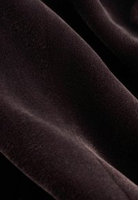 Tumepruun sametkangas pehmea ja siledaga tekstuuriga ning diskreetse läikega; omab õrnu voldikesi ja erinevaid valguse peegeldusi.