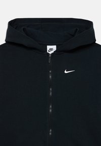 Felpa nera con zip realizzata in tessuto morbido, con tasca a marsupio, cappuccio regolabile con cordino e logo Nike swoosh bianco sul petto.