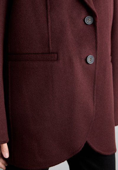 Cappotto in misto lana bordeaux con una texture liscia; presenta due bottoni, una tasca sul petto e un design con orlo curvo.
