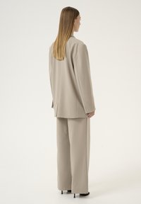 Beige Anzug mit taillierter Passform, bestehend aus einem entspannten Blazer und weiter Hose, gefertigt aus glattem Stoff mit subtiler Textur und ohne sichtbare Muster.