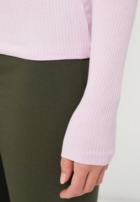 Top de mangas longas em rosa claro com nervuras, combinado com calças justas verdes escuras. Possui um design de manga ajustada com uma ligeira flare no pulso.