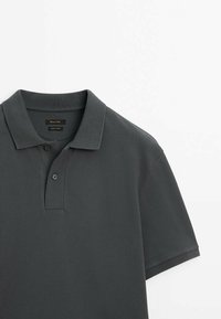 Polo shirt gris foncé avec un tissu texturé, un col rabattable et une patte de boutonnage à trois boutons. Le tissu semble lisse et durable.