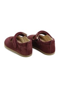 Zapatos Mary Jane de ante rojo con puntera redondeada, correa en el tobillo y suela de goma color beige. Presentan detalles perforados en la parte superior del zapato.