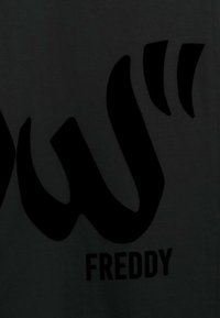 Camiseta negra con un gran diseño gráfico negro de letras estilizadas con la palabra "FREDDY" debajo en un tipo de letra en negrita. Textura suave.