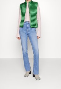 Grønne puffervest med lynlås over en lys pink ribbet sweater, parret med lyseblå lige ben jeans og grå hæled ankelstøvler.