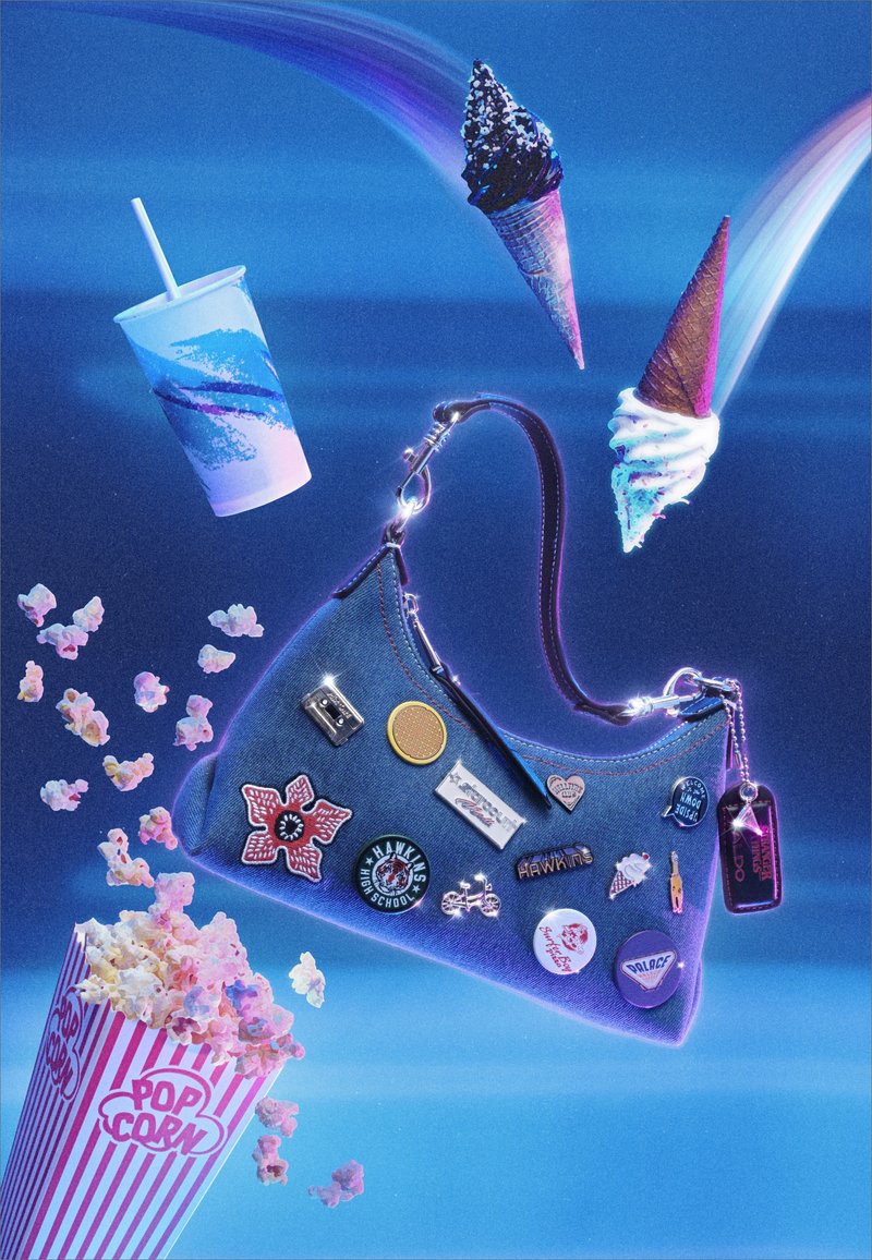 Denim shoulder bag with pins floating among popcorn, a soft drink cup, and two ice cream cones against a blue background with rainbow light trails.