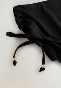 Črne kratke hlače iz tkanine z elastičnim pasom, vrvico z zlatim okrasnim biserom in gladko, lahko teksturo.