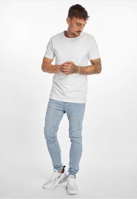 Valkoinen puuvillapaita, vaaleansiniset skinny-farkut ja valkoiset lenkkarit. Ominaisuuksina monimutkaiset tatuoinnit käsivarsilla ja tiukka muotoilu.