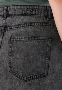 Sorte denimjeans med en baklomme med subtil søm og en livrem preget med "2NDDAY." Stoffet har en lett tekstur.