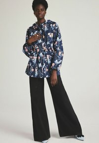 Floral-patterned hooded jacket in navy with cinched waist. Paired with wide-legged black pants and light blue shoes.