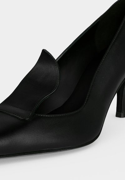 Chaussure à talon haut en cuir noir à bout pointu avec un détail de rabat plié sur la tige et un talon fin.