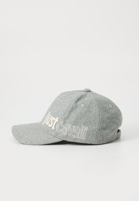 Sivina tkanina baseball kapa s izvezenim natpisom "Just Cavalli" v beli barvi na strani, prikazana na enostavni beli podlagi.