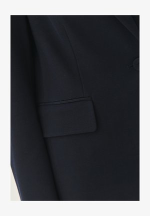 Blazer en tissu navy avec revers en notch, fermeture à un bouton, et une poche passepoilée avec des coutures soignées et une texture lisse.