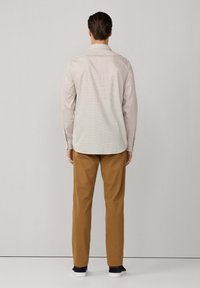 Camisa a cuadros de colores claros con mangas largas, combinada con pantalones marrones ajustados y zapatillas oscuras, vista desde atrás.