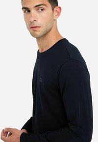 Maglietta a maniche lunghe colore blu navy con scollatura rotonda e un logo discreto sul petto. La texture liscia e il design aderente migliorano il comfort e lo stile.