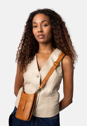 Chaleco sin mangas beige con solapa, combinado con un bolso de cuero marrón tipo bandolera que cuenta con un bolsillo frontal y una correa ajustable.