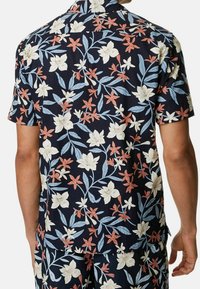 Kortärmad skjorta i marinblått med blommönster som har vita, ljusblå och korallfärgade blommor. Lättviktig tyg, avslappnad passform, knappstängd krage.