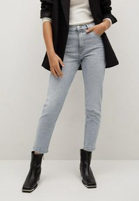 Jasnoniebieskie spodnie z wysokim stanem o slim fit, w zestawieniu z czarnymi botkami za kostkę i czarną marynarką, charakteryzujące się gładką teksturą i klasycznym fasonem.