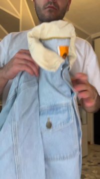 Homme tenant une veste en jean bleu clair avec un col en shearling crème et une étiquette orange à l'intérieur, à l'intérieur.