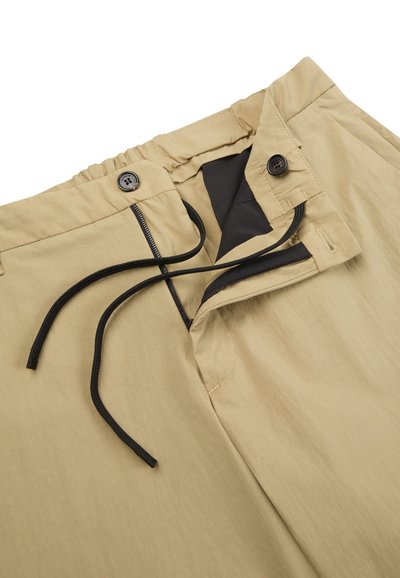 Beige lightweight pants with an elastic waistband, two buttons, a drawstring, and a dark fabric lining inside the waistband.