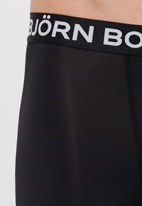 Čierne spodné prádlo s širokým elastickým pásom, na ktorom sú biele písmená "BJÖRN BORG". Materiál je hladký a mierne lesklý.