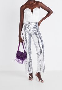 Body blanc sans bretelles avec un décolleté en forme de cœur, associé à un pantalon évasé orné de sequins argentés brillants. Sac à franges violet et talons métalliques.