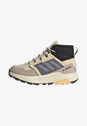 Zapatos de senderismo de corte medio en color beige y negro, con parte superior de malla, suela de goma y una destacada marca de tres rayas en gris. Presentan un diseño texturizado.