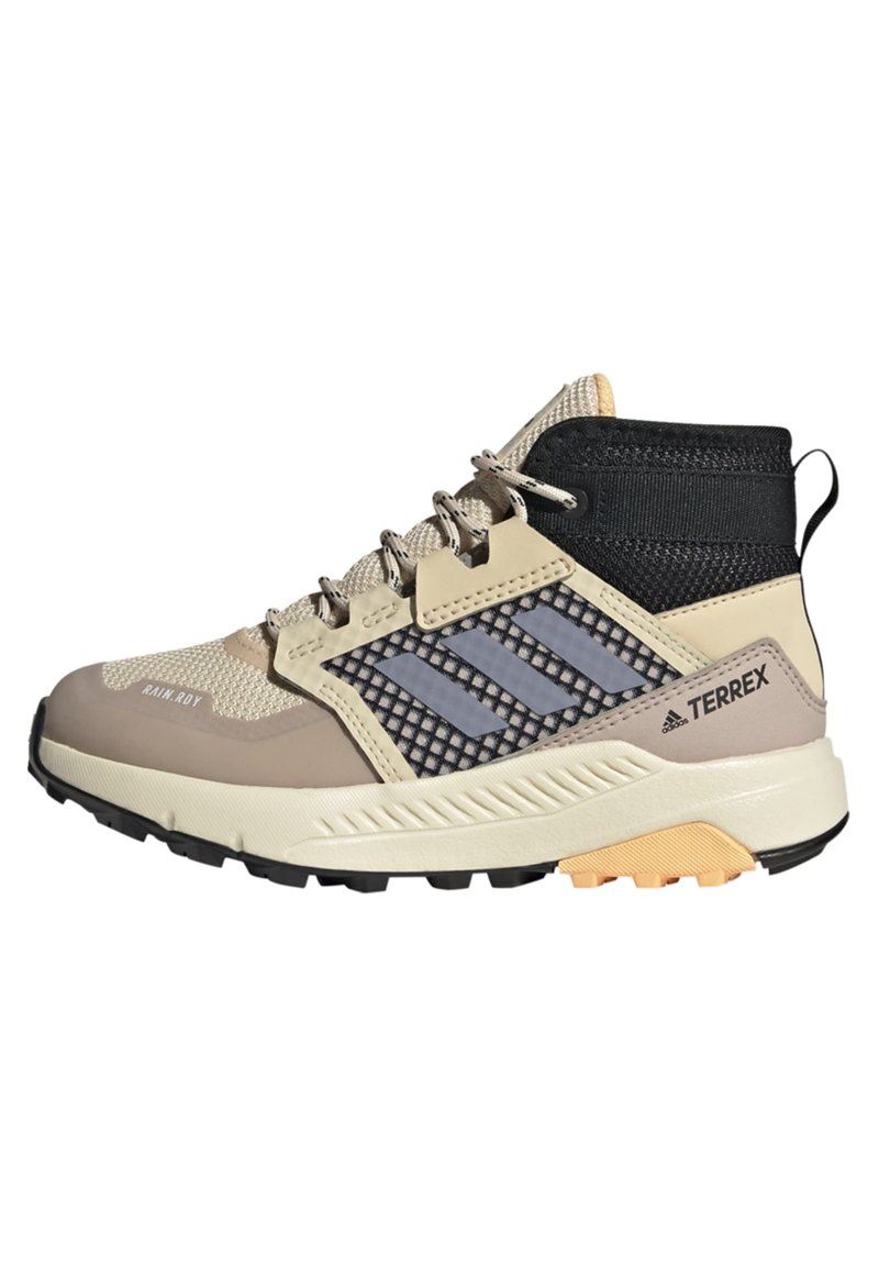 Zapatos de senderismo de corte medio en color beige y negro, con parte superior de malla, suela de goma y una destacada marca de tres rayas en gris. Presentan un diseño texturizado.