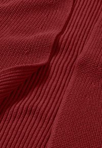 Rotes Strickgewebe mit unterschiedlichen Texturen, das gerippte und glatte Bereiche zeigt und ein weiches, warmes Erscheinungsbild hervorhebt.